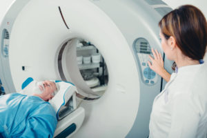 an older male patient sits in a scanner while a female nurse to the right operates it